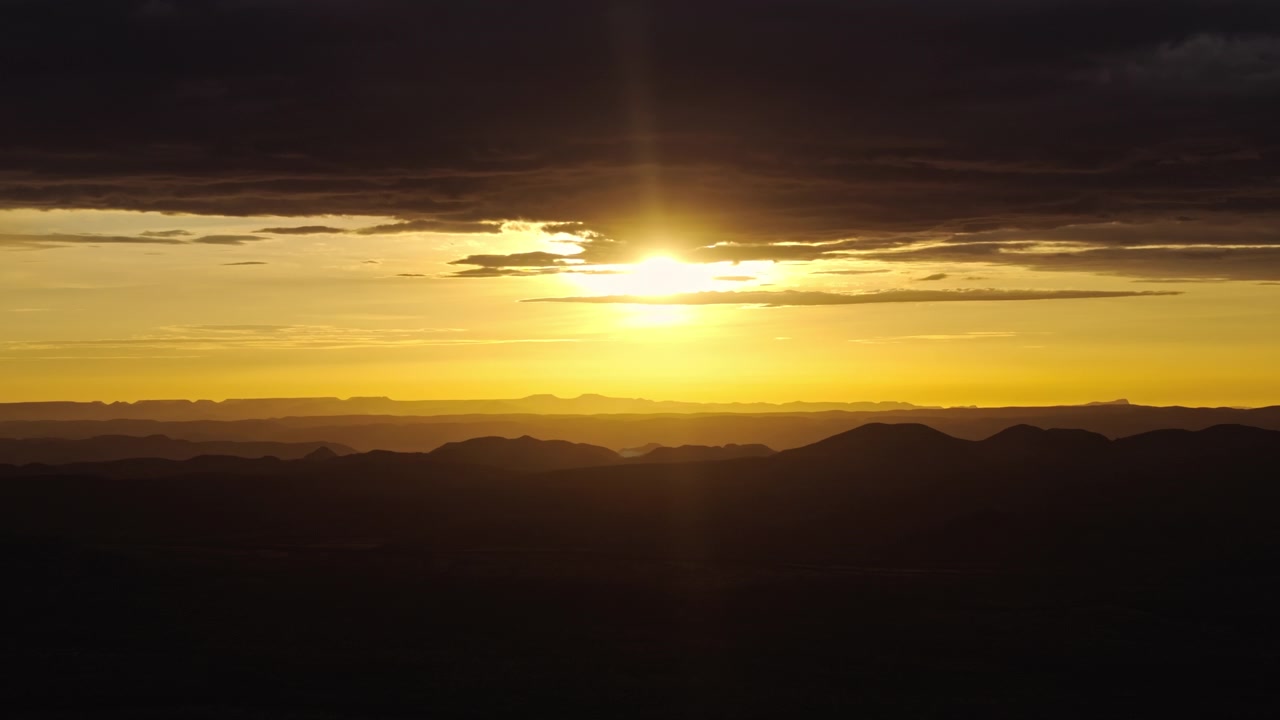 Aerial view of a radiant sunburst over silhouetted desert mountains in central Namibia, golden rays flaring across a dramatic evening sky.