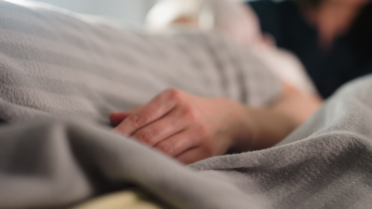 Female client lies relaxed on spa bed under soft light with hand resting on blanket during massage therapy session promoting skin comfort and relaxation in serene indoor spa environment