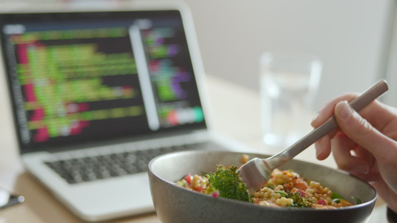 cerca de un hombre comiendo un almuerzo vegano saludable en el escritorio de la oficina mientras usa una computadora portátil