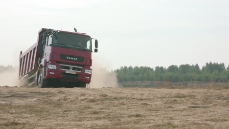 camión de descarga kamaz rojo conduciendo a través de un campo polvoriento