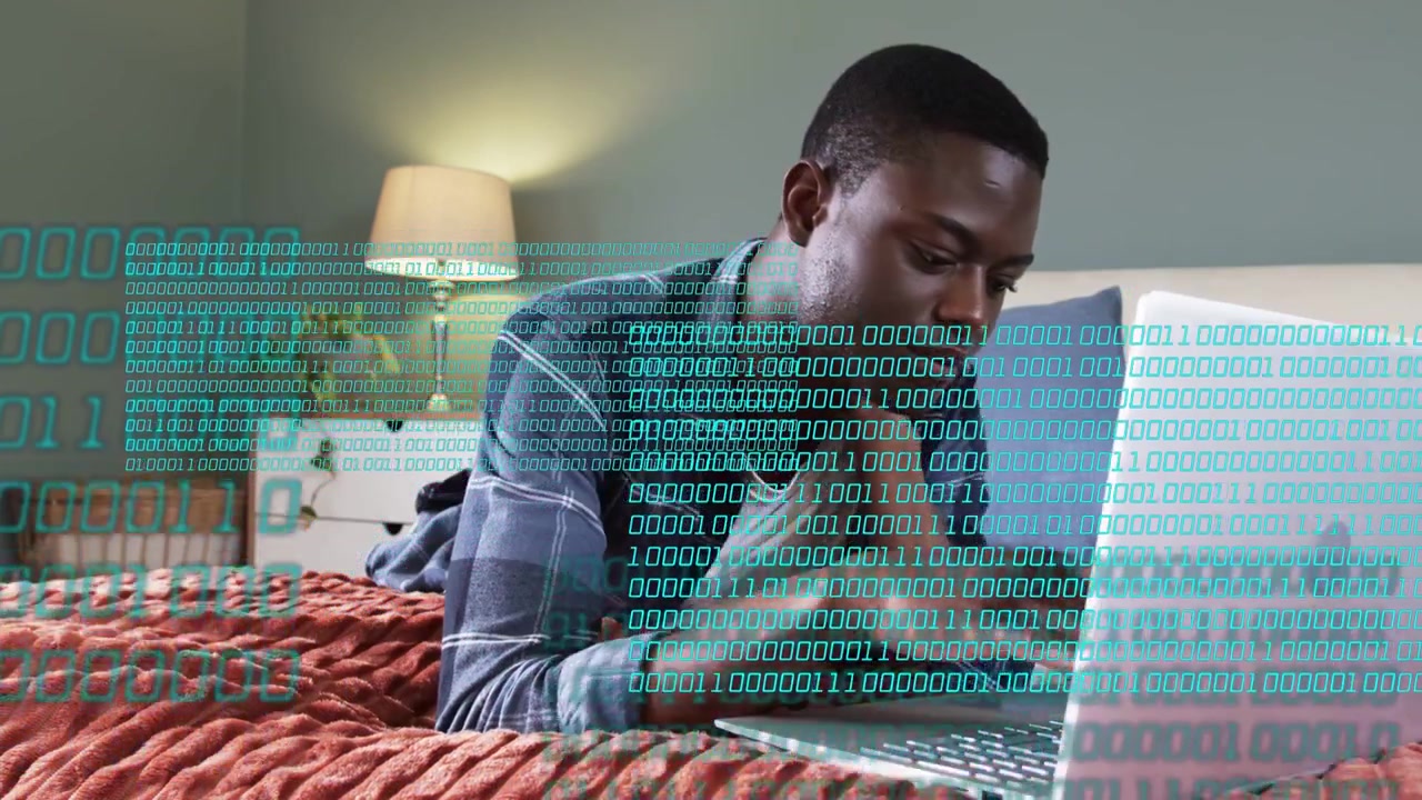 Man opening laptop in bed reading and typing while binary overlay growing obscuring hands for work