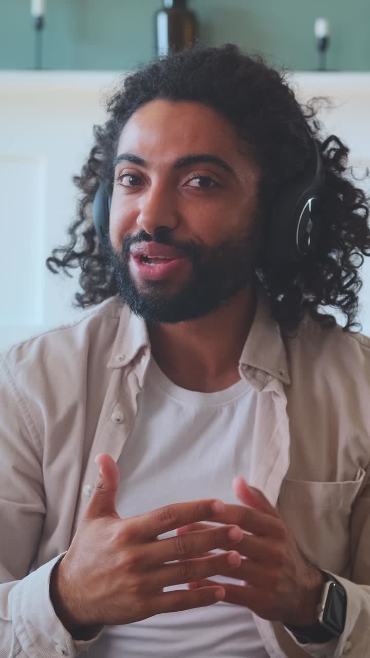 Young casual arabian man in headphones talks and gestures looking at screen