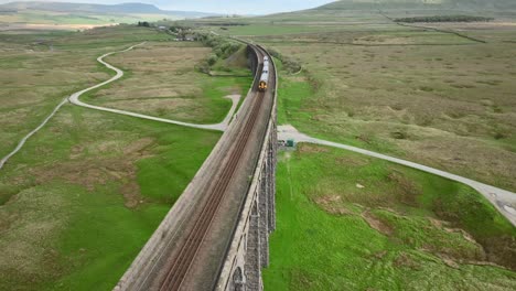 Passenger-train-crossing-curved-railway-viaduct-bridge-and-traveling-under-reversing-drone-camera