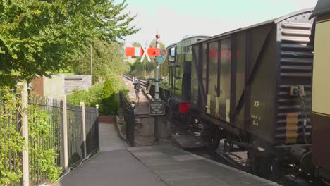 historic steam train waiting in east somerset railway station with signal and trees nearby