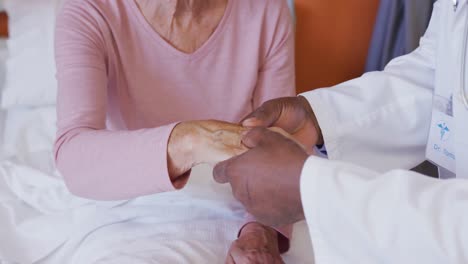 African-american-male-doctor-examining-the-hand-of-senior-caucasian-female-patient-at-hospital