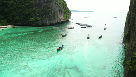 barcos tradicionales asiáticos de madera que navegan por las aguas turquesas de la bahía de pi leh, tailandia