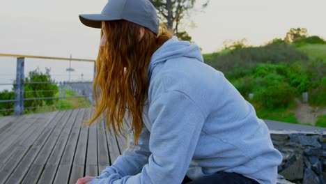 side view of young caucasian female skateboarder sitting on skateboard at observation point 4k