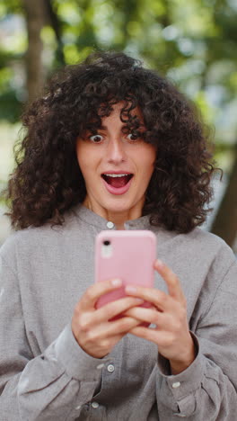feliz excitada mujer joven caucásica usar teléfono inteligente celebrando ganar buenas noticias mensaje en la calle de la ciudad