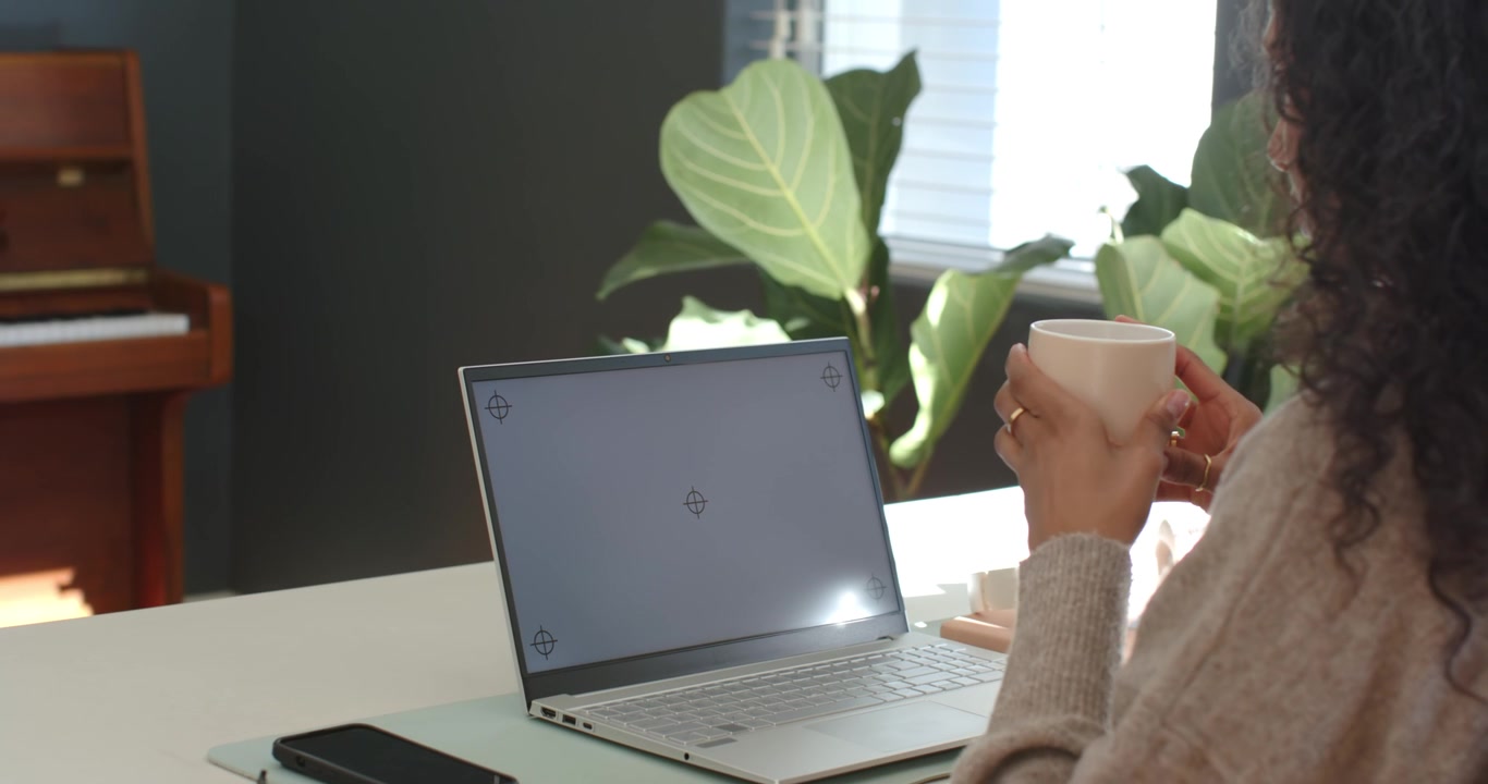Una donna entra nell'inquadratura con una tazza alla scrivania, si avvicina al laptop e si prepara a sorseggiare
