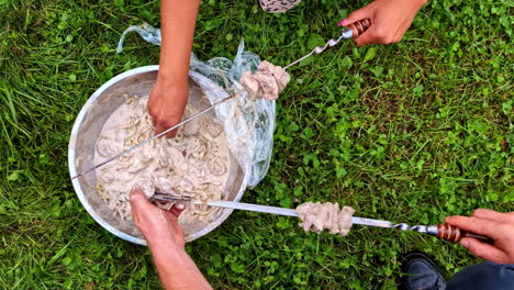 people dip meat into creamy marinade for shish kebabs in a grassy area