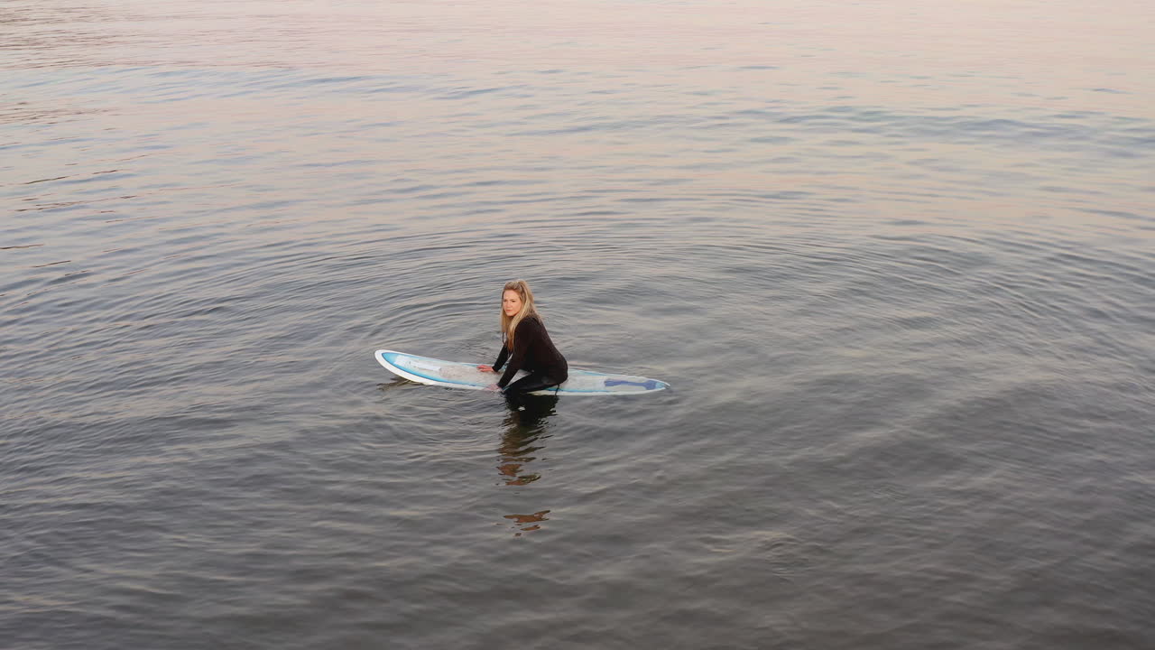 fotografía de un avión no tripulado de una mujer con traje de buceo sentada en una tabla de surf en el mar