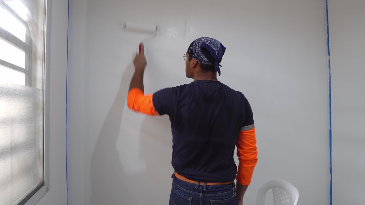 trabajador masculino pinta la pared usando un pintor de rodillos - de cerca