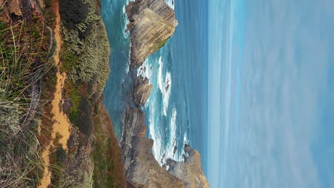 Praia-de-Almograve-beach-with-ocean-waves,-cliffs-and-stones,-wet-golden-sand-and-green-vegetation-at-wild-Rota-Vicentina-coast,-Odemira,-Portugal