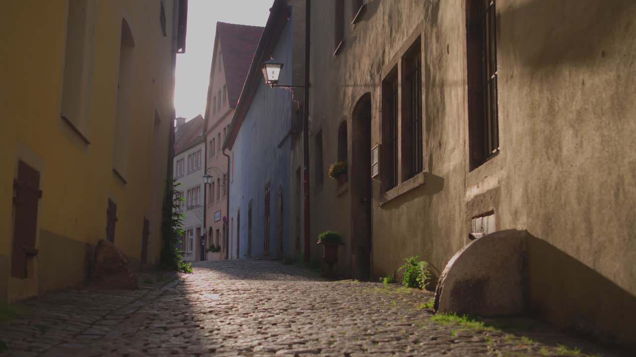 Early morning sunlight is illuminating an empty cobblestone alley with colorful buildings in Rothenburg ob der Tauber, Germany