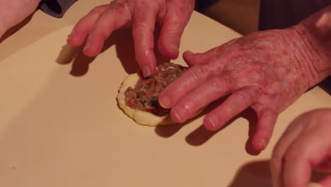 grandmother senior hands preparing small pizza-like bread with ground beef topping, esfiha dish