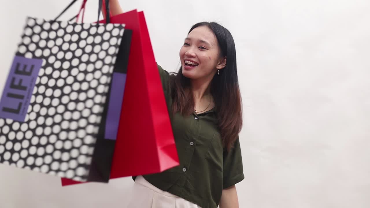 Cheerful Asian woman holding shopping bags. Isolated on white background