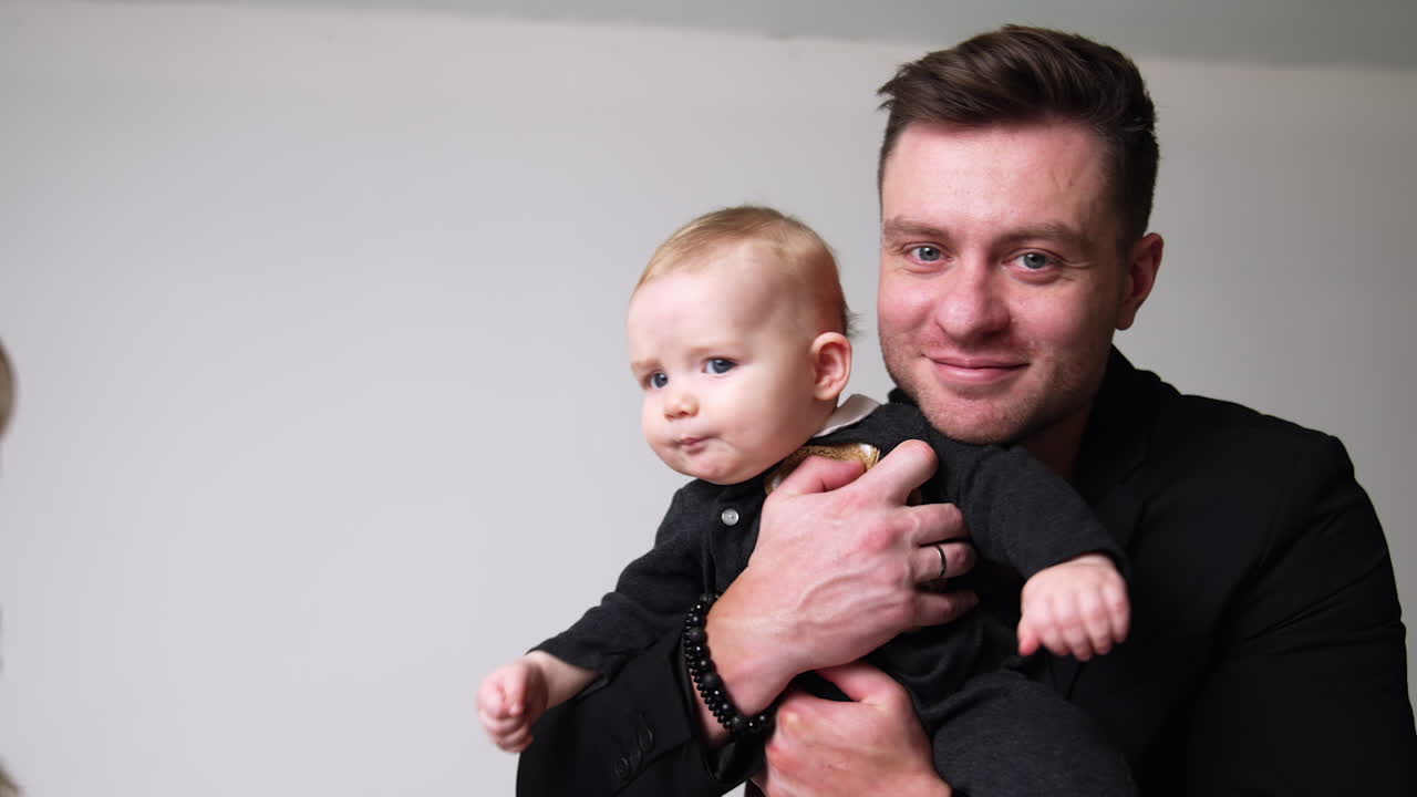 Muscular man and his adorable baby boy. Beautiful woman comes up to her man and son embracing them lovingly. Parents kiss their child on the cheek.