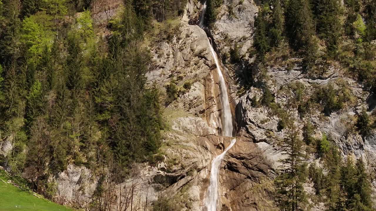 Drone in ascesa che rivela un'alta cascata di montagna circondata da una foresta di conifere e scogliere rocciose a Klöntal, Glarona, Svizzera.