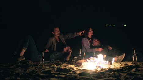 dos parejas lindas abrazándose y sentadas junto a la hoguera tarde en la noche mirando las estrellas