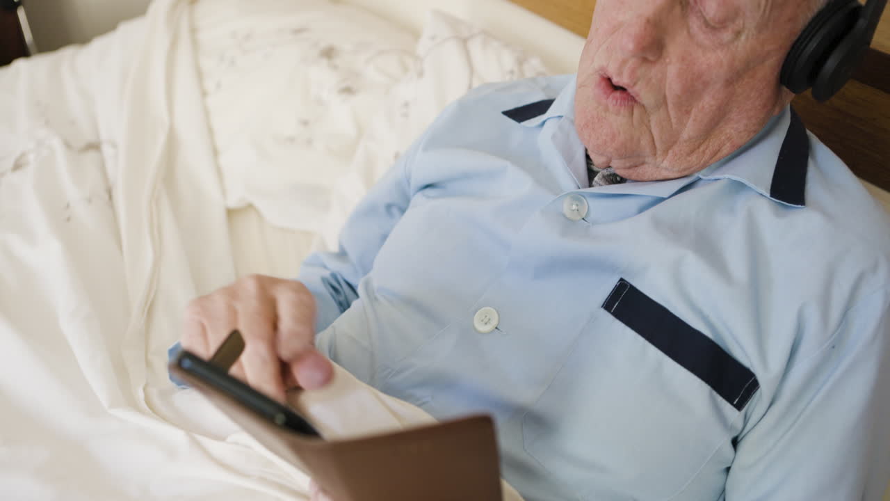 Elderly man relaxing in bed with headphones