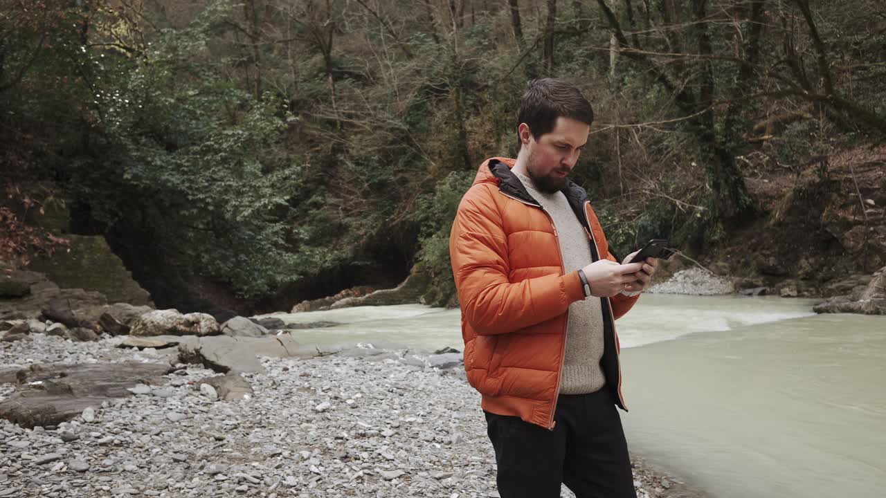 Uomo che usa il telefono in riva a un fiume in una foresta