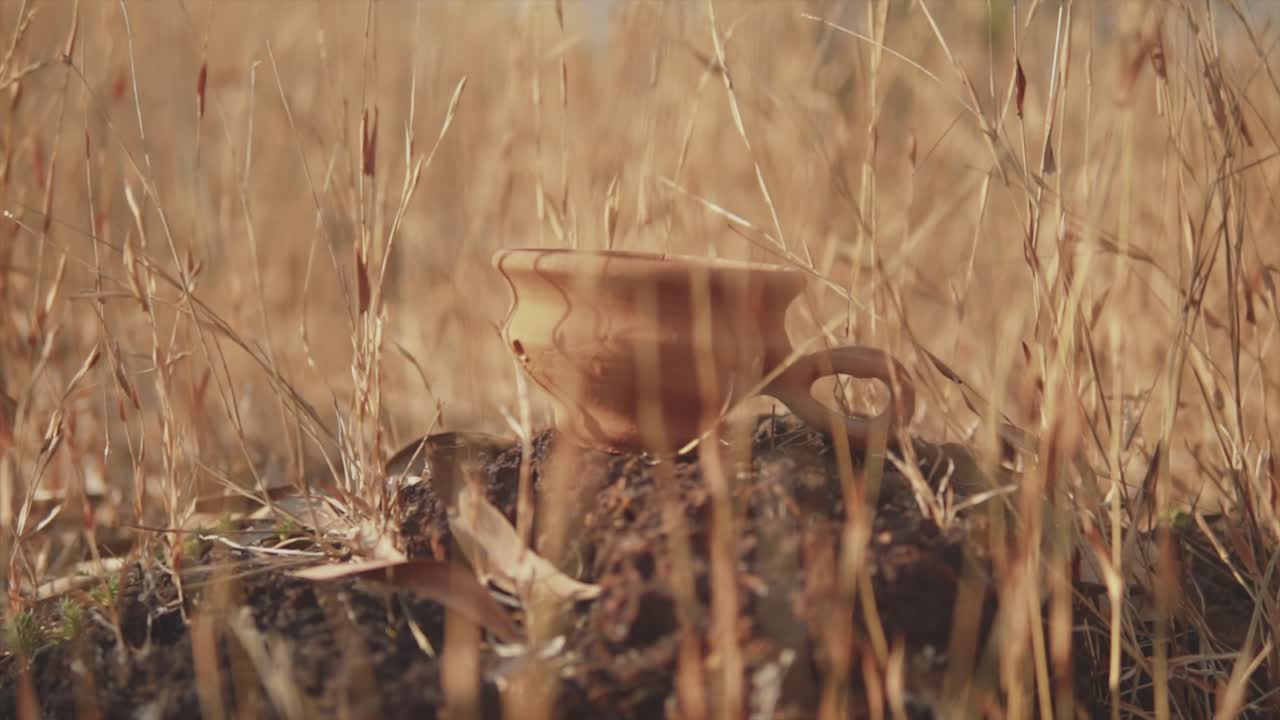 들판의 마른 풀로 둘러싸인 뜨거운 태양 아래 바위에 손잡이가 달린 아름다운 점토 냄비의 클로즈업 샷