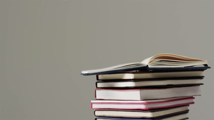 Primo piano di un libro aperto su una pila di libri su sfondo grigio, al rallentatore