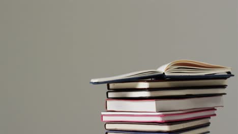 Close-up-of-open-book-on-stack-of-books-on-grey-background,-in-slow-motion