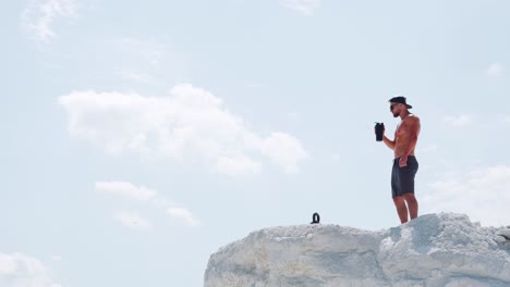 fitness trainer drinks water from a bottle. male athlete on the mountain against the sky. outdoor sports training