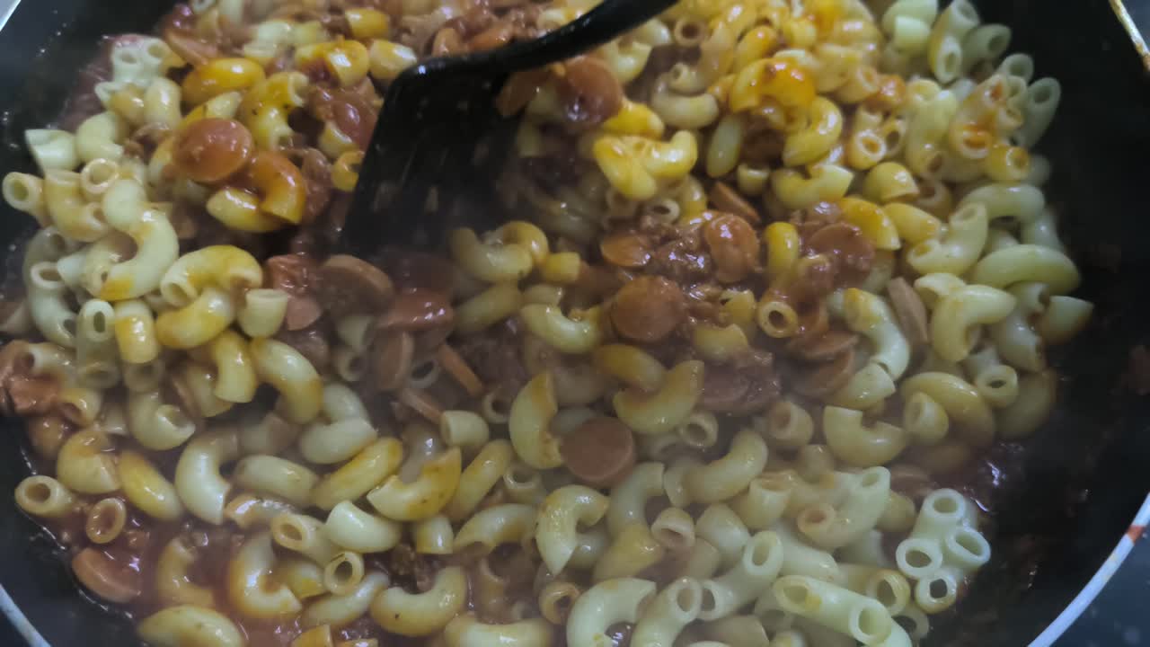 A chef is cooking macaroni in a pan, mixing it with a pre-made sauce. The bubbling mixture looks delicious and appetizing. This preparation highlights the cooking process