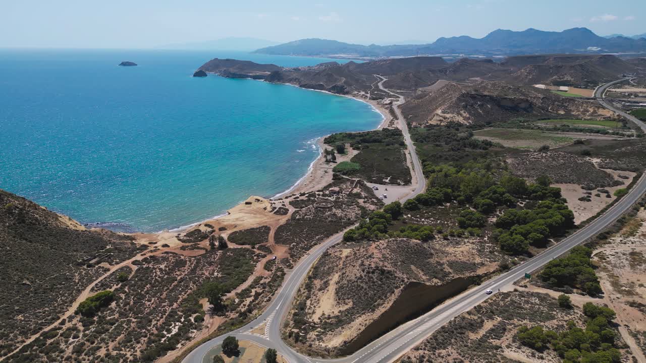 Aerial view of a winding coastal road near Águilas in the Murcia region of Spain, revealing beaches, rugged hills and turquoise Mediterranean waters along the southeast shoreline