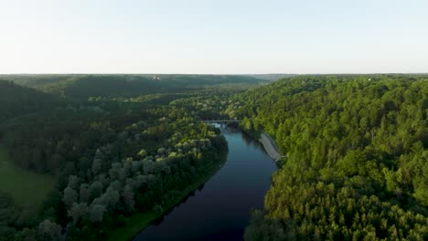 an aerial view a sunny summer evening the gauja river flows between green forests and a bridge crosses the river