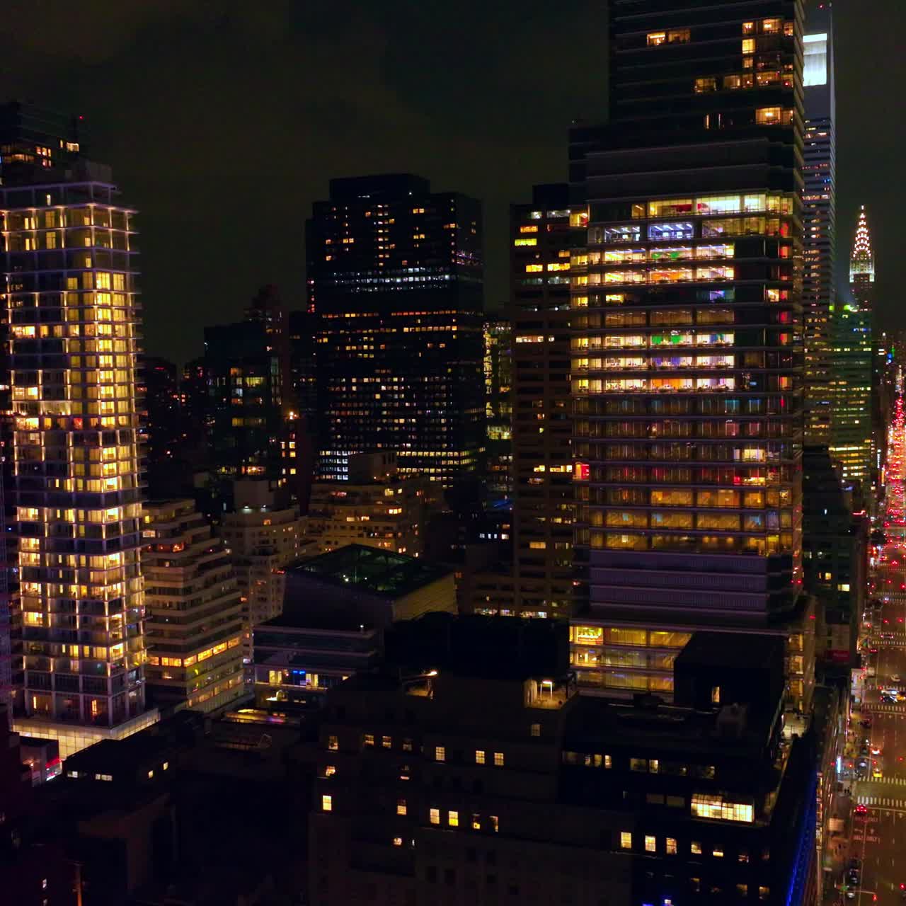 Long street with busy traffic passing through the amazing architecture. Fantastic skyscrapers with lights in windows at night