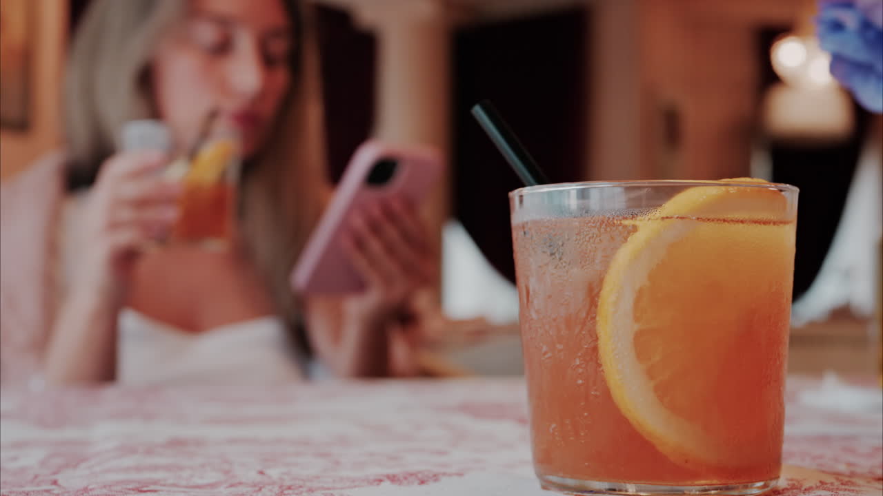 Close up of an orange cocktail on a table with a woman on the background at a restaurant