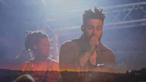 male singer and percussionist playing music on dim stage with haze, lighting rig and sunset overlay