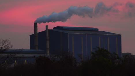 Un-Edificio-De-Fábrica-Industrial-Con-Una-Gran-Tubería-Que-Emite-Humo-Contra-El-Fondo-Rosa-Del-Cielo-Del-Atardecer-En-Da-Nang,-Vietnam