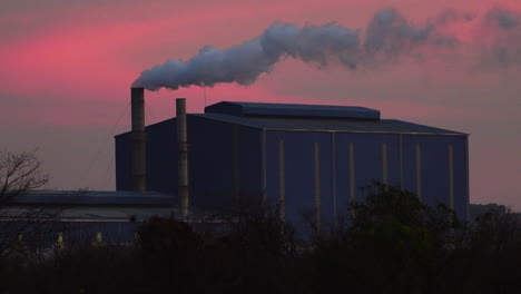 un edificio de fábrica industrial con una gran tubería que emite humo contra el fondo rosa del cielo del atardecer en da nang, vietnam