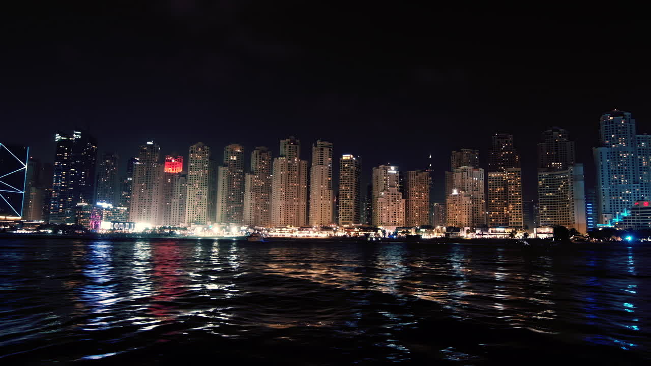 A panoramic view of Dubai Marina's skyline at night, where tall residential towers are mirrored on the calm water surface