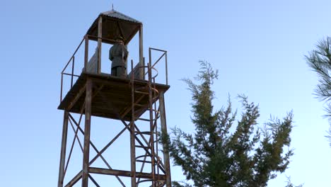 wide shot of a uniformed army soldier up in a watch tower