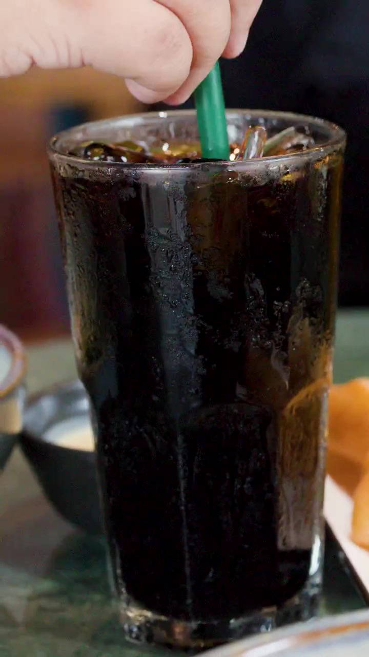 Primo piano della mano di un bambino che mescola caffè freddo con una cannuccia verde prima di sollevare il bicchiere