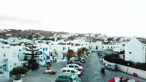 vista aérea de tres personas que viajan por la ciudad en bicicleta en las hermosas calles vacías de mykonos con autos estacionados afuera de casas blancas tradicionales