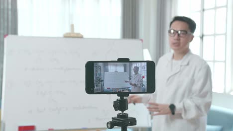 close up of smartphone camera recording asian male teacher with glasses teaching chemist at home