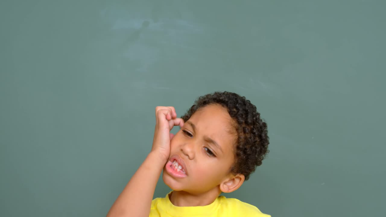Front view of thoughtful African American schoolboy standing against chalkboard in classroom 4k