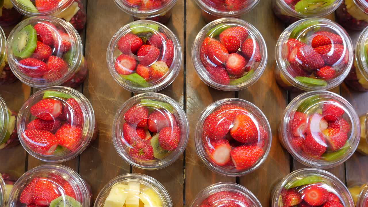 filas de deliciosas tazas de frutas: fresas, kiwi, piña y granada