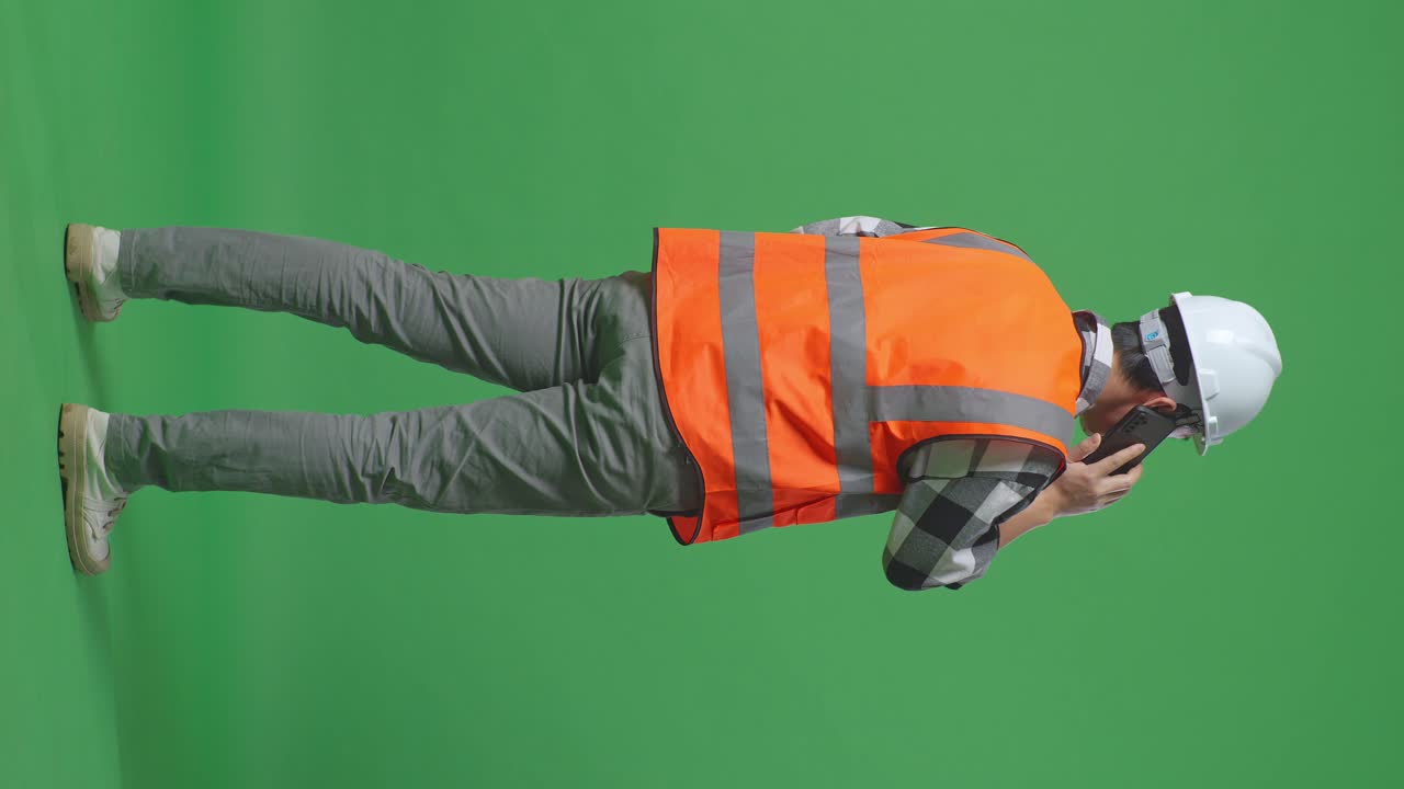 Full Body Back View Of Asian Male Engineer With Safety Helmet Talking On Smartphone While Standing In The Green Screen Background Studio