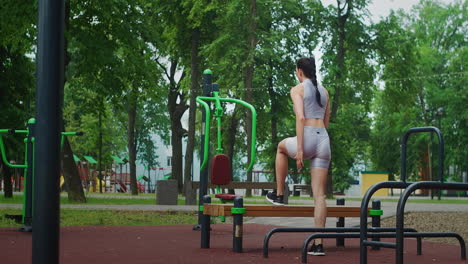 una mujer joven en un parque realiza estocadas en un banco en ropa deportiva en el verano. atletismo mujer caucásica entrena en el parque.