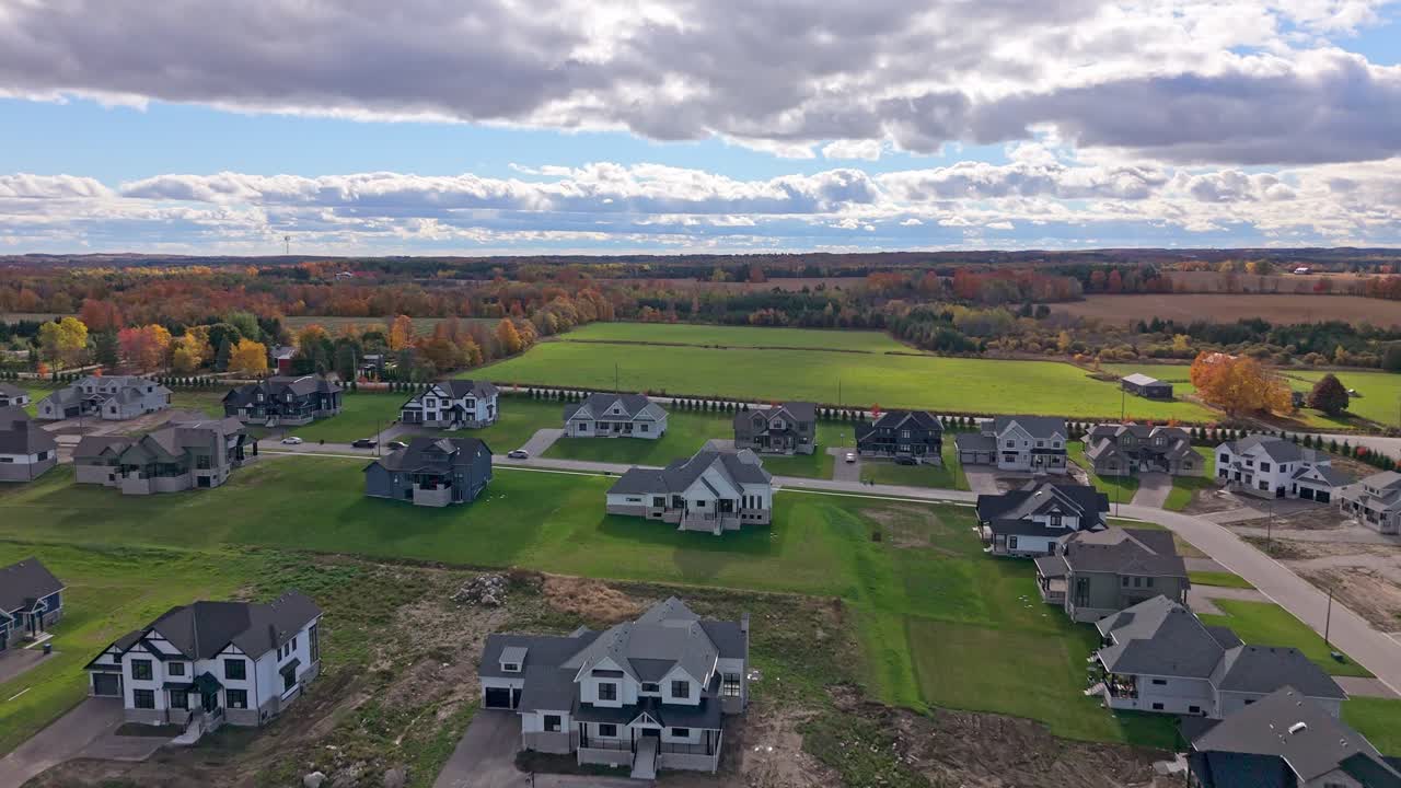 Dron klouže nad novou čtvrtí v Altonu, Caledonu, Ontario, s rodinnými domy, zelenými trávníky a zemědělskou půdou v pozadí pod dramatickými podzimními mraky