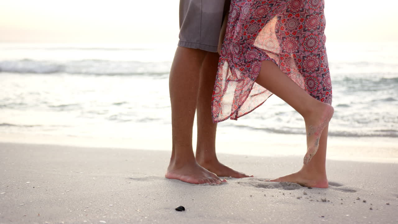 una pareja descalza está cerca en una playa de arena, con una mujer en un vestido estampado