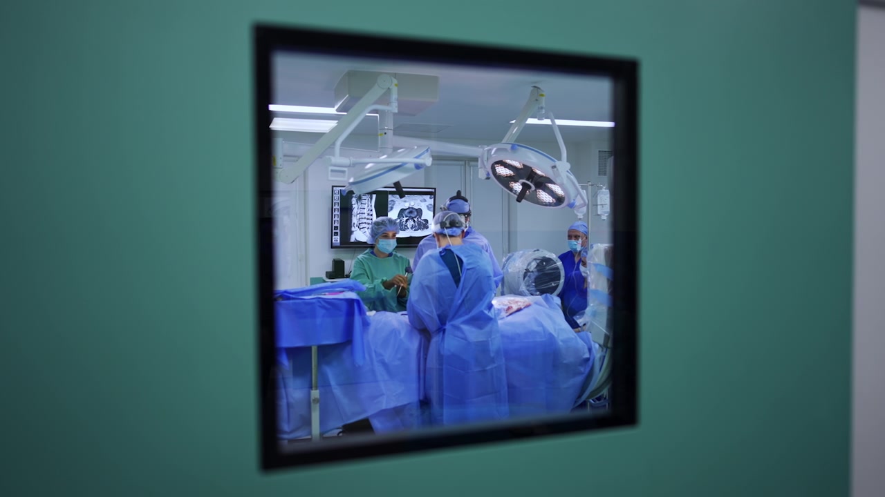 Mirando un quirófano moderno a través de la ventana cuadrada de la puerta. El equipo médico trabaja en la operación dentro.