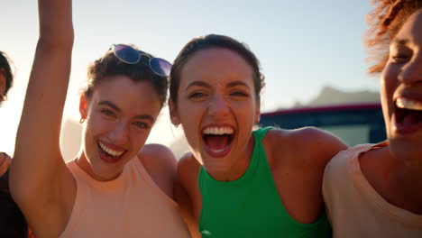 portrait of laughing female friends standing by open top car on road trip